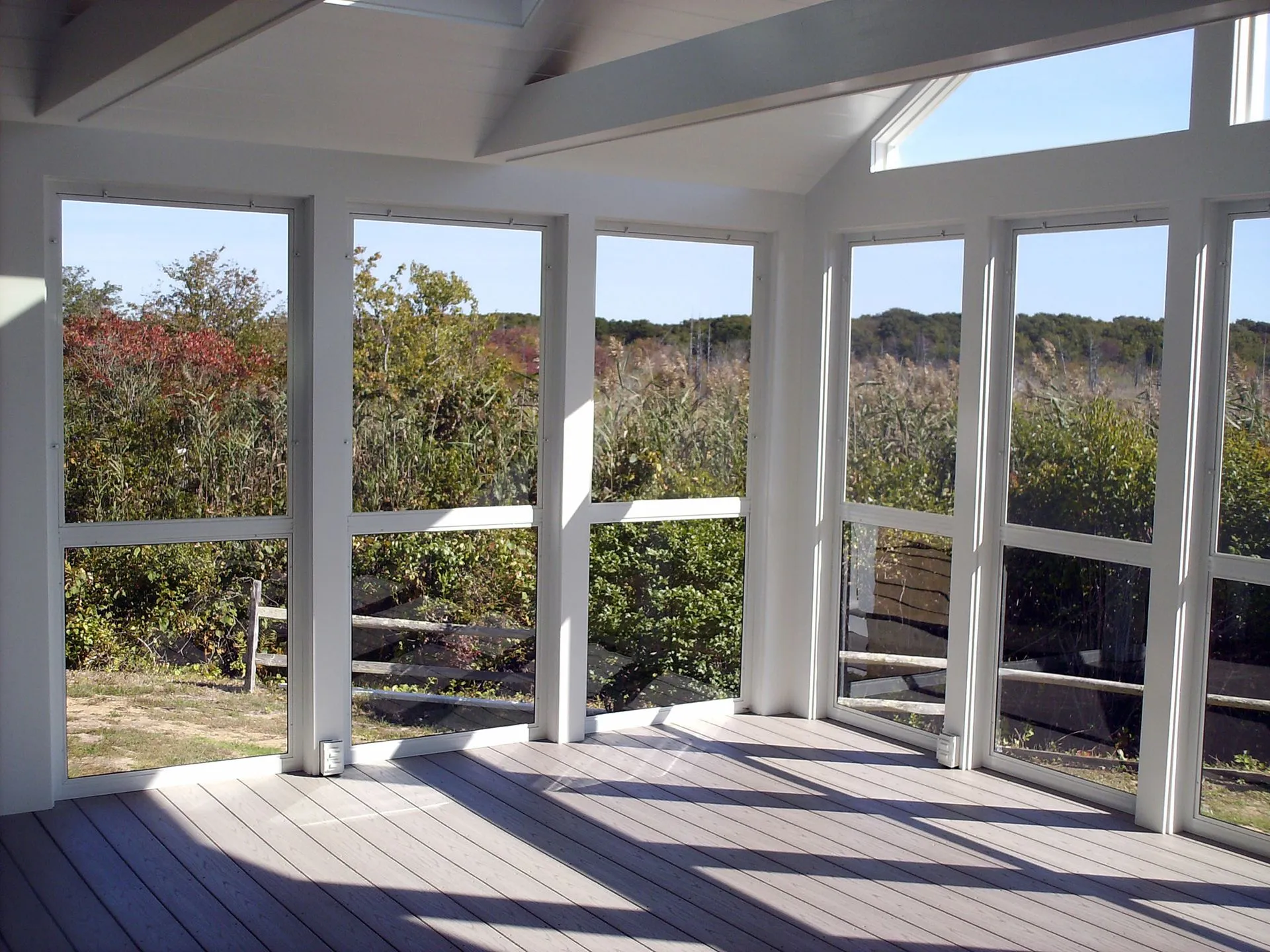 a screened in porch with a fence and trees in the background