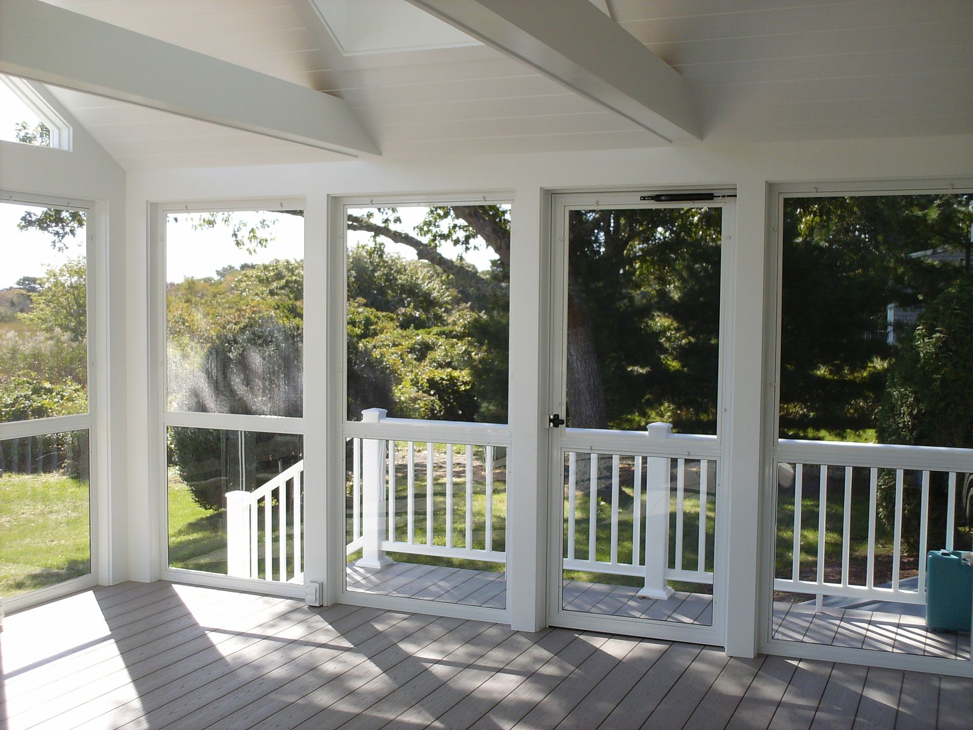 a screened in porch with a deck and trees in the background